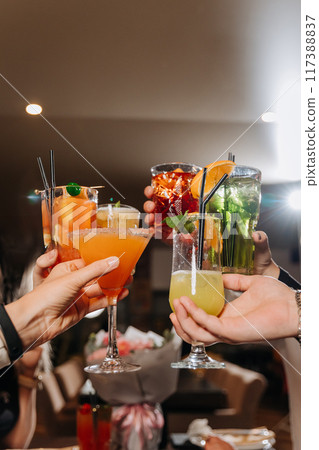 Group of friends toasting with cocktails in a vibrant bar setting, celebrating togetherness 117388837