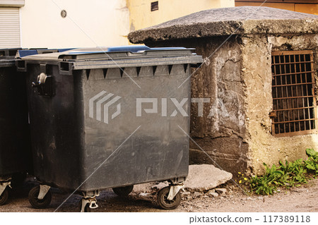 Black garbage container standing outside near the aged ventilation hut in evening sepia tones 117389118