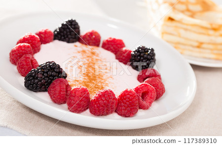 Breakfast of raspberries and blackberries with yogurt and pancakes on table Breakfast of raspberries and blackberries with yogurt and pancakes on table 117389310