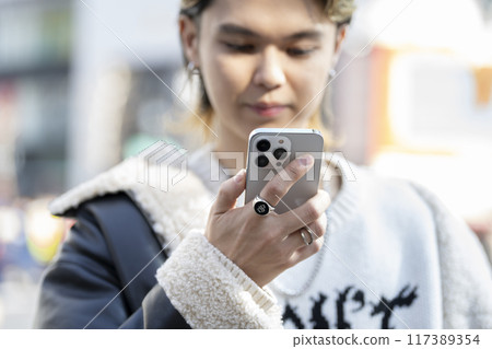 The hands of a young man operating a smartphone in the city 117389354
