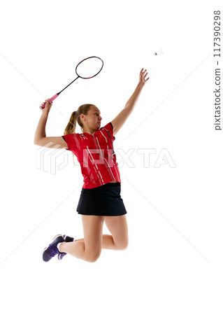 Young girl, badminton athlete, jumping in mid-air to hit shuttlecock, repulse enemy attack against white studio background. 117390298