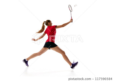 Side view photo of young woman in uniform with rocket, badminton player leaping to hits shuttlecock against white studio background. 117390384