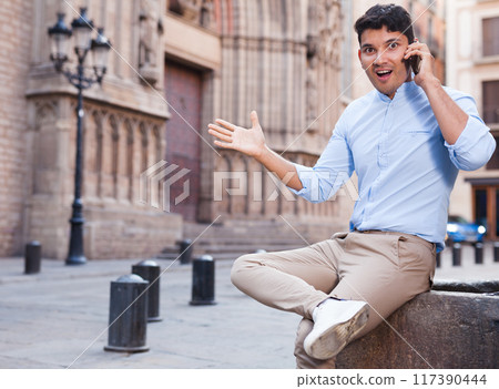 Modern guy walks in city and communicates on smartphone Modern guy walks in city and communicates on smartphone 117390444