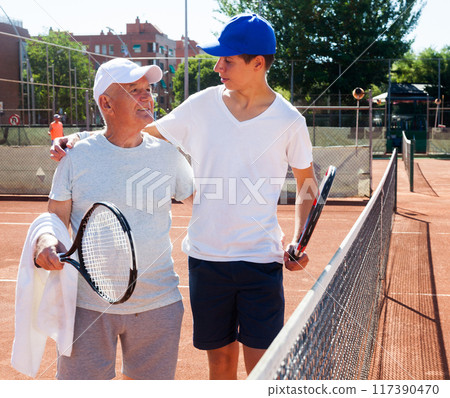 Grandfather and grandson talking on court playing tennis 117390470