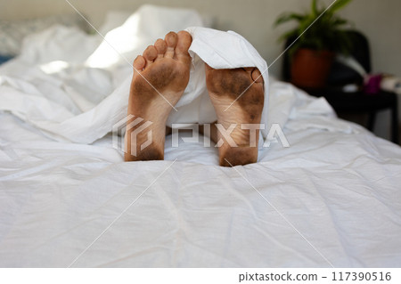 A Relaxing Morning with Cozy Bare very dirty Feet Resting Comfortably Under a Soft Bedcover 117390516