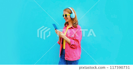 Portrait of stylish modern happy smiling young woman in headphones listening to music with phone 117390731