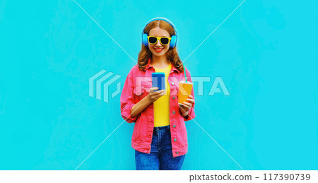 Portrait of stylish modern happy smiling young woman in headphones listening to music with phone 117390739