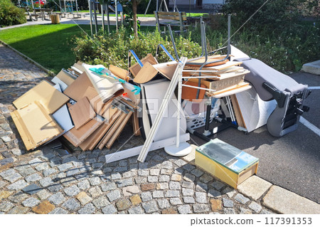 A heap of assorted discarded household items and furniture piled up on a cobblestone street, depicting a bulk waste collection day in an urban environment. 117391353