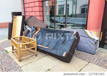 A pile of discarded furniture including a sofa, chair, and various cushions on a city sidewalk, highlighting urban waste and the need for proper disposal or recycling. A pile of discarded furniture including a sofa, chair, and various cushions on a city sidewalk, highlighting urban waste and the need for proper disposal or recycling. 117391363