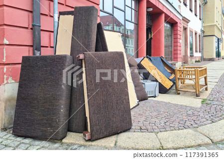Discarded household items including dismantled couch and bamboo chair abandoned on street, reflecting urban waste and the need for proper furniture disposal. Collection, removal of thrown furniture. 117391365
