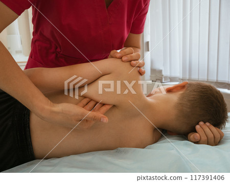 Osteopathy Treatment. Boy's body being manipulated by real kinesio therapist and osteopathic physician. Naturopath treats kid with osteopathy as alternative medicine and therapy. Osteopath harmonizes Osteopathy Treatment. Boy's body being manipulated by real kinesio therapist and osteopathic physician. Naturopath treats kid with osteopathy as alternative medicine and therapy. Osteopath harmonizes 117391406