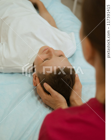 Osteopathy Treatment. Boy's head being manipulated by real osteopathic physician. Naturopath treats kid with osteopathy as alternative medicine and therapy. Osteopath harmonizes body 117391415