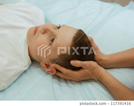 Osteopathy Treatment. Boy's head being manipulated by real osteopathic physician. Naturopath treats kid with osteopathy as alternative medicine and therapy. Osteopath harmonizes body 117391416