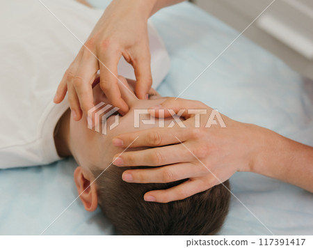 Osteopathy Treatment. Boy's head being manipulated by real osteopathic physician. Naturopath treats kid with osteopathy as alternative medicine and therapy. Osteopath harmonizes body 117391417