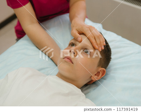 Osteopathy Treatment. Boy's forehead being manipulated by real osteopathic physician. Naturopath treats kid with osteopathy as alternative medicine and therapy. Osteopath harmonizes body 117391419