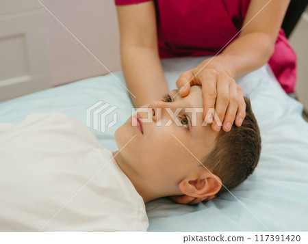 Osteopathy Treatment. Boy's forehead being manipulated by real osteopathic physician. Naturopath treats kid with osteopathy as alternative medicine and therapy. Osteopath harmonizes body Osteopathy Treatment. Boy's forehead being manipulated by real osteopathic physician. Naturopath treats kid with osteopathy as alternative medicine and therapy. Osteopath harmonizes body 117391420