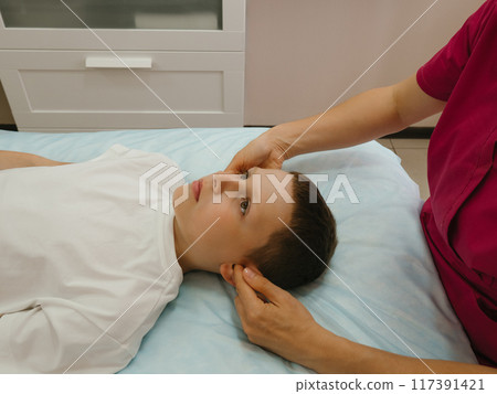 Osteopathy Treatment. Boy's ears being manipulated by real osteopathic physician. Naturopath treats kid with osteopathy as alternative medicine and therapy. Osteopath harmonizes body Osteopathy Treatment. Boy's ears being manipulated by real osteopathic physician. Naturopath treats kid with osteopathy as alternative medicine and therapy. Osteopath harmonizes body 117391421