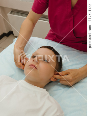 Osteopathy Treatment. Boy's ears being manipulated by real osteopathic physician. Naturopath treats kid with osteopathy as alternative medicine and therapy. Osteopath harmonizes body 117391422