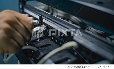 Male network administrator inserts cables into the server rack Male network administrator inserts cables into the server rack 117391438