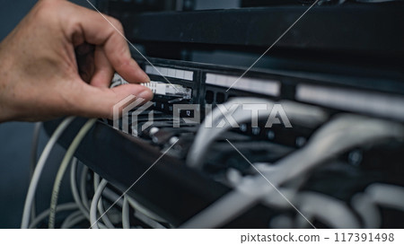Male system administrator connects cables with server rack working in server room Male system administrator connects cables with server rack working in server room 117391498