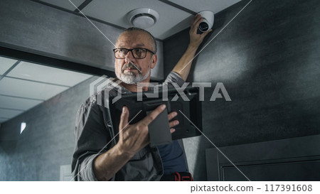 Male technician uses tablet computer to set up surveillance camera in office room Male technician uses tablet computer to set up surveillance camera in office room 117391608