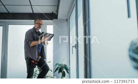 Male technician stands on ladder, installs CCTV camera in office room using tablet Male technician stands on ladder, installs CCTV camera in office room using tablet 117391715