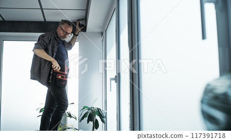 Male technician screws security camera to the ceiling in office 117391718
