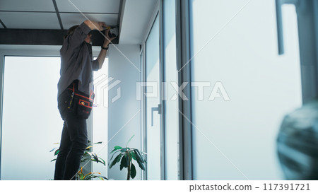 Male technician screws security camera to the ceiling in office Male technician screws security camera to the ceiling in office 117391721