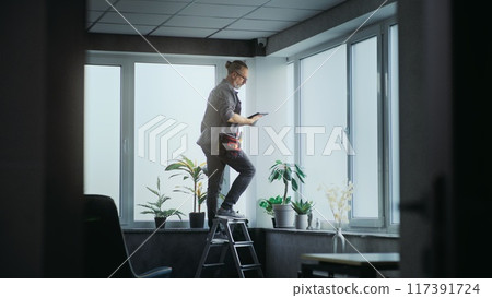 Male installer stands on ladder and screws surveillance camera to the ceiling 117391724