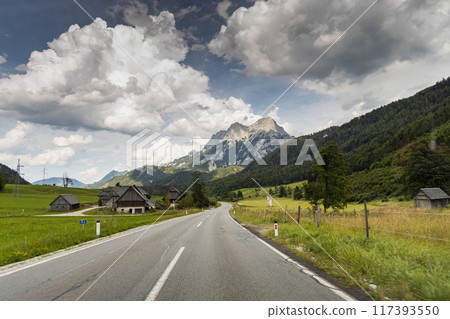 Asphalt road with mountain and heavy clouds on background and cottages on foreground, Austrian Alps 117393550