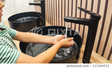 Boy washing hands under clean water on black sink 117394531