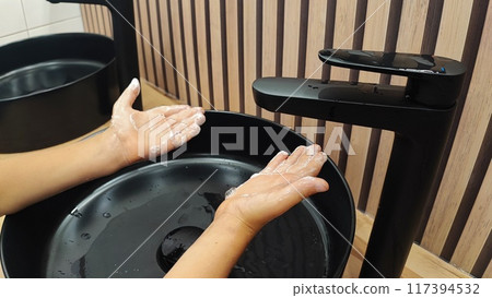 Boy washing hands under clean water on black sink 117394532