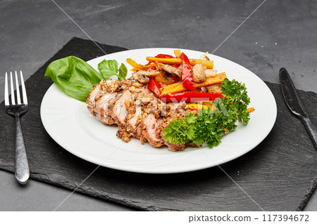 Tender sliced meat with roasted vegetables and fresh herbs on a white plate 117394672