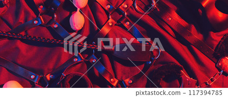 set of BDSM sex toys with handcuffs, a whip flogger and a mask for submission and domination on a red background 117394785