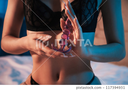 silicone butt anal plug in the hands of a woman girl with a sexy body in underwear sitting on bed in bedroom. Female sex toys for anal sex and orgasm 117394931