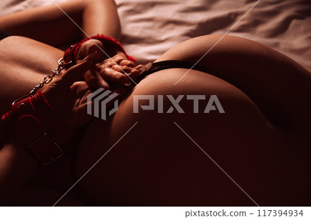 submissive sexy woman with hands in BDSM handcuffs with beautiful ass in panties lies on bed in bedroom. Slave girl with a slender naked body for BDSM sex with submission and domination 117394934