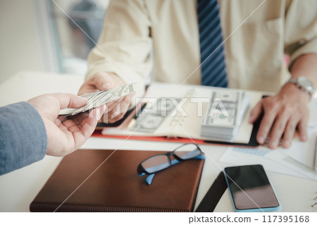 Man offering batch of hundred dollar bills. Hand of a businessman giving money to his partner. Hand receiving money from businessman. Venality, bribe, corruption concept. Man offering batch of hundred dollar bills. Hand of a businessman giving money to his partner. Hand receiving money from businessman. Venality, bribe, corruption concept. 117395168