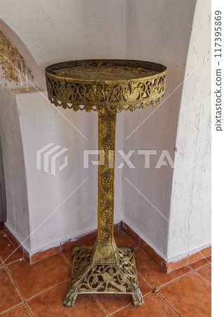 Ornate golden candelabra candle holder stand with intricate motifs, before a wall. 117395869