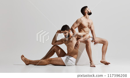 Two men in white shorts rest, one seated on block, other reclining with arm extended, both displaying calm and contemplative demeanor. 117396208