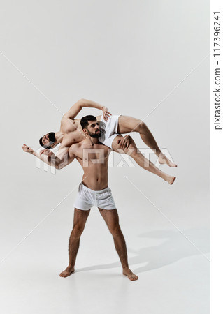 Powerful display of strength as one wrestler effortlessly lifts his opponent, showcasing skill and control against warm grey background. Powerful display of strength as one wrestler effortlessly lifts his opponent, showcasing skill and control against warm grey background. 117396241
