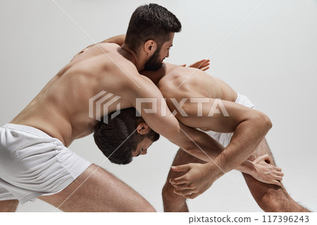 Two competitors, equally matched, wrestle in test of strength and willpower, both seeking to outmaneuver other against warm grey background. 117396243