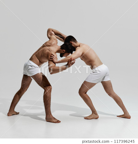 Dynamic wrestling duel unfolds, with two competitors locked in struggle for dominance and victory against warm grey background. Dynamic wrestling duel unfolds, with two competitors locked in struggle for dominance and victory against warm grey background. 117396245