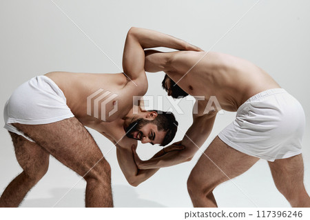 Two men, athletes grapple, showcasing their strength and technique against warm grey studio background. Two men, athletes grapple, showcasing their strength and technique against warm grey studio background. 117396246