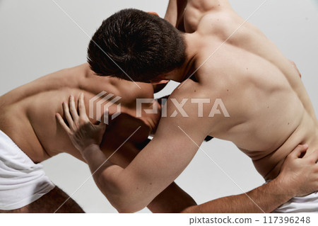 Intense wrestling bout between two strong men, determined competitors dressed underwear against warm grey background. Intense wrestling bout between two strong men, determined competitors dressed underwear against warm grey background. 117396248