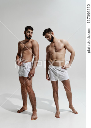 Two brunette, bearded, young men, with athletic bodies posing in underwear shows his physique against warm grey background. Two brunette, bearded, young men, with athletic bodies posing in underwear shows his physique against warm grey background. 117396250