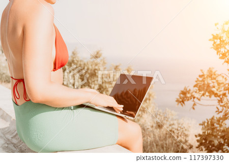 Woman laptop park. Working remotely on seashore. Happy successful woman female freelancer working on laptop at summer sunset, makes a business transaction online. Freelance, remote work on vacation 117397330