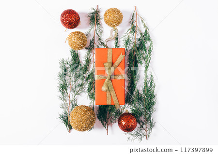 A red box with a gold ribbon sits on a table with Christmas decorations 117397899
