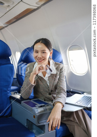 A woman is sitting on an airplane with a laptop open in front of her A woman is sitting on an airplane with a laptop open in front of her 117398068
