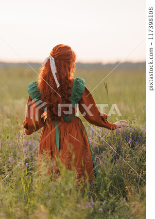 A shepherdess woman with red hair and a green dress sits in a field of flowers. A shepherdess woman with red hair and a green dress sits in a field of flowers. 117398108