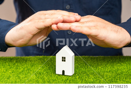 A man protects a house figurine with his hands. Concept of property protection and guarding. Property and real estate insurance against potential risks and damages. Security systems A man protects a house figurine with his hands. Concept of property protection and guarding. Property and real estate insurance against potential risks and damages. Security systems 117398235